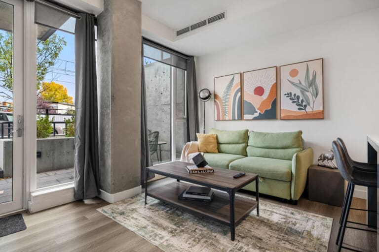 Living room with green sofa and patio door to a walkout terrace in a 1-bedroom Calgary condo