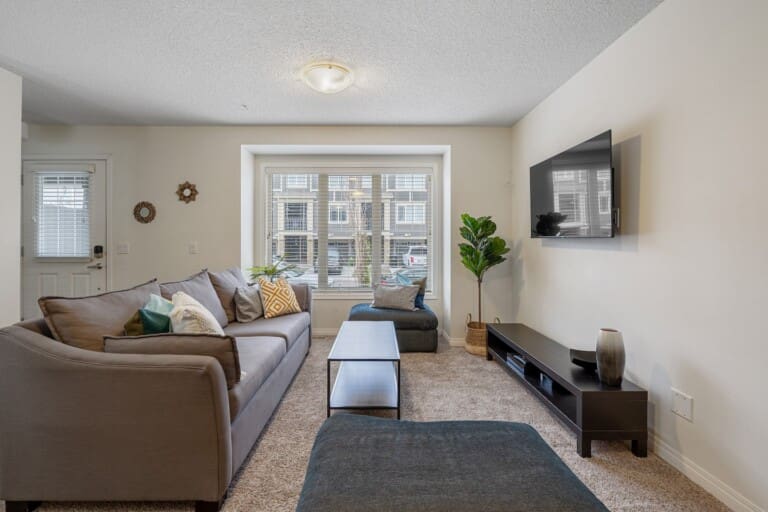 Living room with brown sofa and large front window in a 3-bedroom Calgary row home
