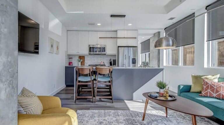 Open-plan living area with teal sofa and white kitchen with breakfast bar in a Calgary walkout suite