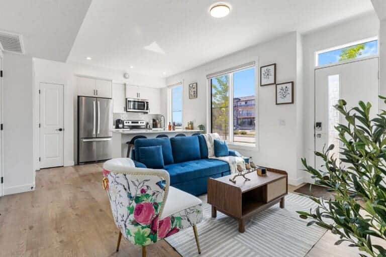 Living room with blue sofa, floral armchair and open kitchen in a 1-bedroom Seton, Calgary suite