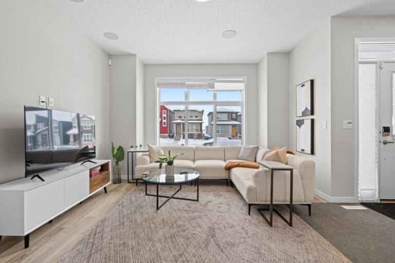 Living room with cream sectional and large front window in a 4-bedroom Livingston, Calgary home