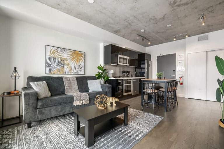 Living room with grey sofa, concrete ceiling and kitchen in a high-floor Calgary condo