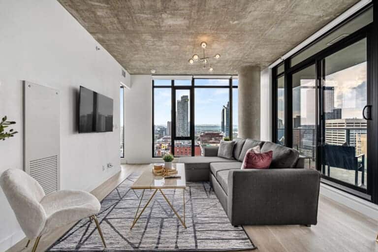 Living room with grey sectional, concrete ceiling and floor-to-ceiling city views in Calgary