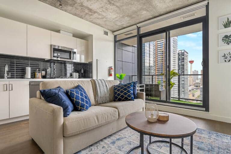 Living room with beige sofa, kitchen and balcony with tower views in a 1-bedroom Calgary condo