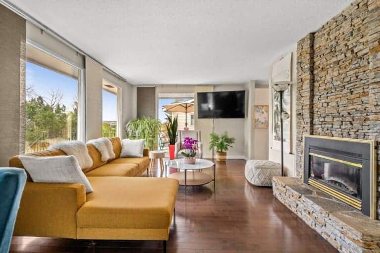 Living room with mustard sectional, stone fireplace and large windows in a 3-bedroom Calgary home