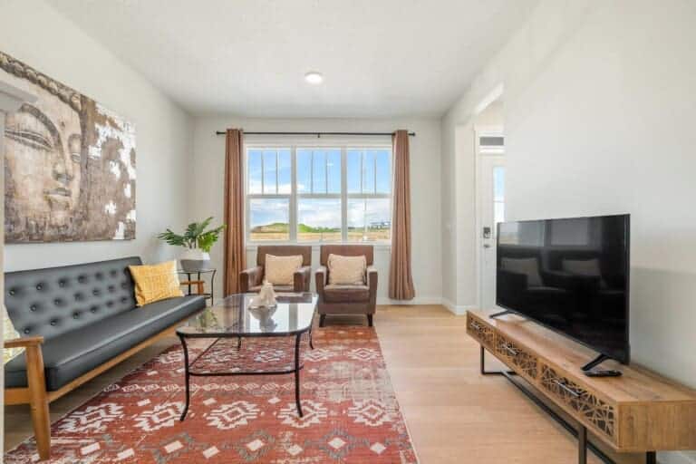 Living room with leather sofa, patterned rug and large window in a new 4-bedroom Calgary home