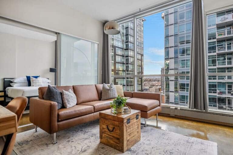 Living room with tan leather sofa and floor-to-ceiling windows in a 2-bedroom Calgary condo