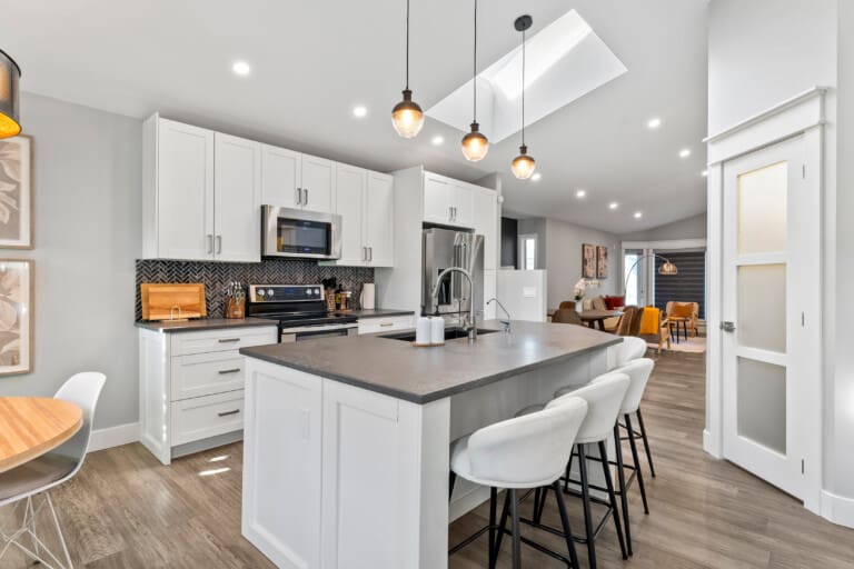 Kitchen with white cabinets, large island, bar stools and skylight in a 4-bedroom Calgary home