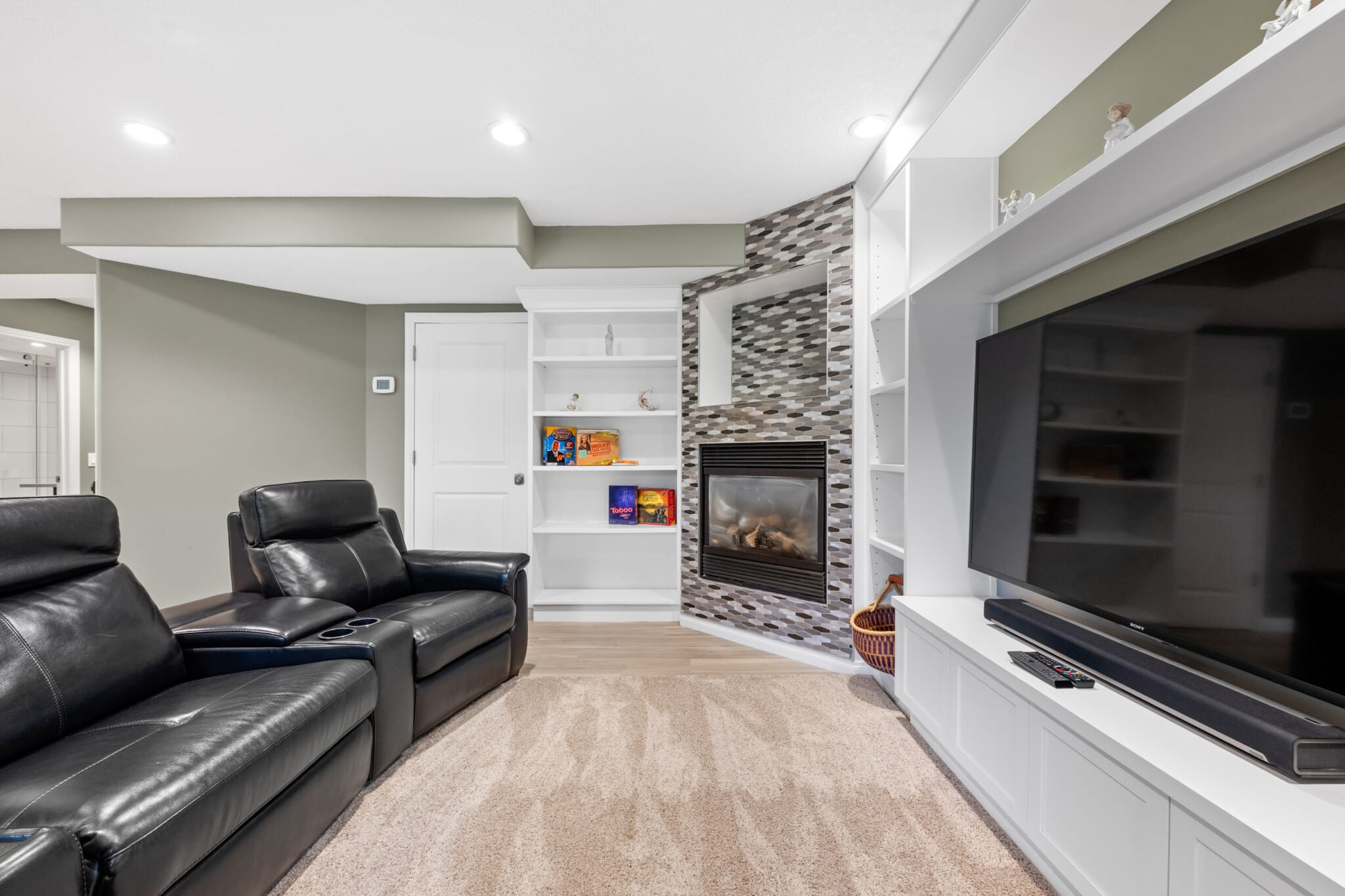 Living room with leather recliners, fireplace and large TV in a private Evergreen suite near Fish Creek, Calgary
